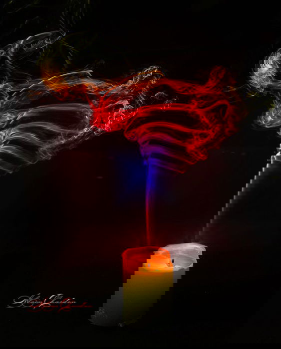 A vivid candle is being blown out by a swirl of rainbow-colored smoke. 