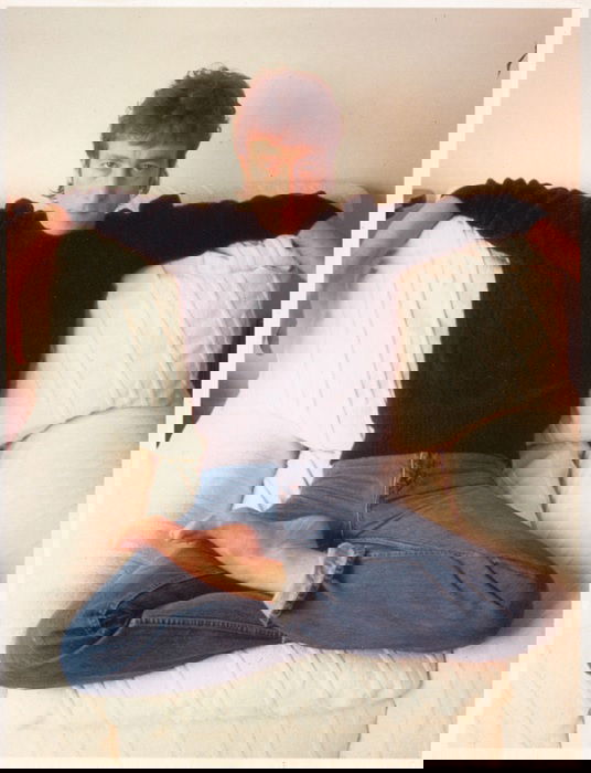 portrait of John Lennon sitting crossed legged on a white couch 